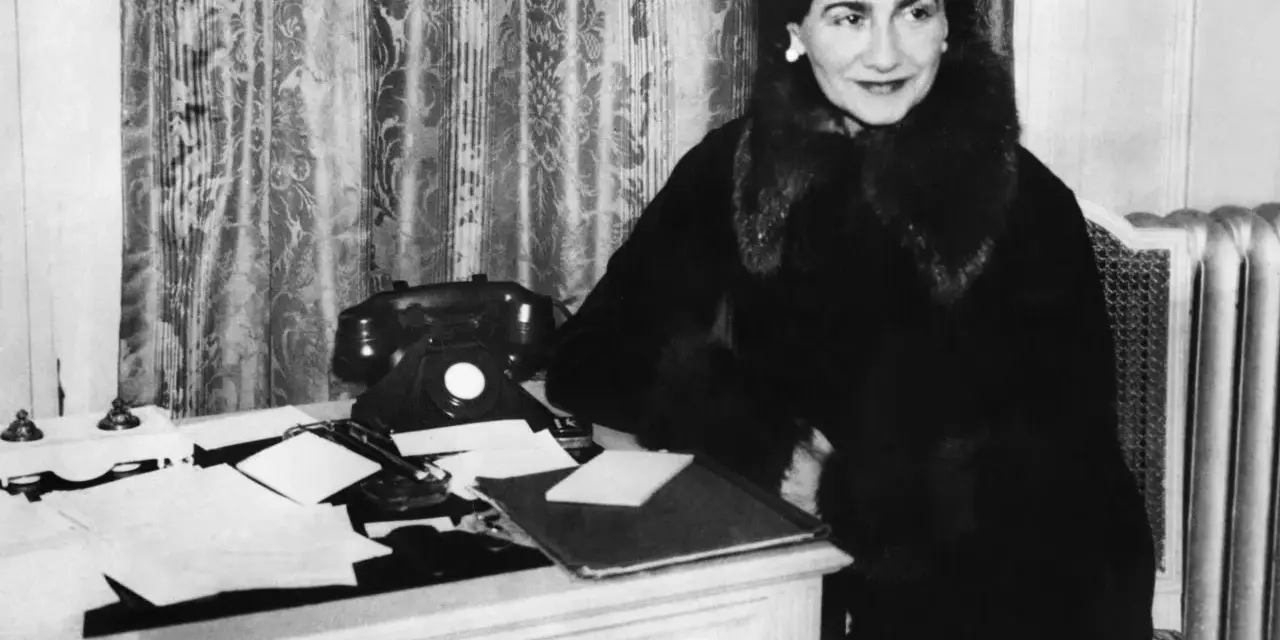 Coco Chanel, icona di stile, al suo scrittoio. La sua storia è fatta di eleganza e innovazione.