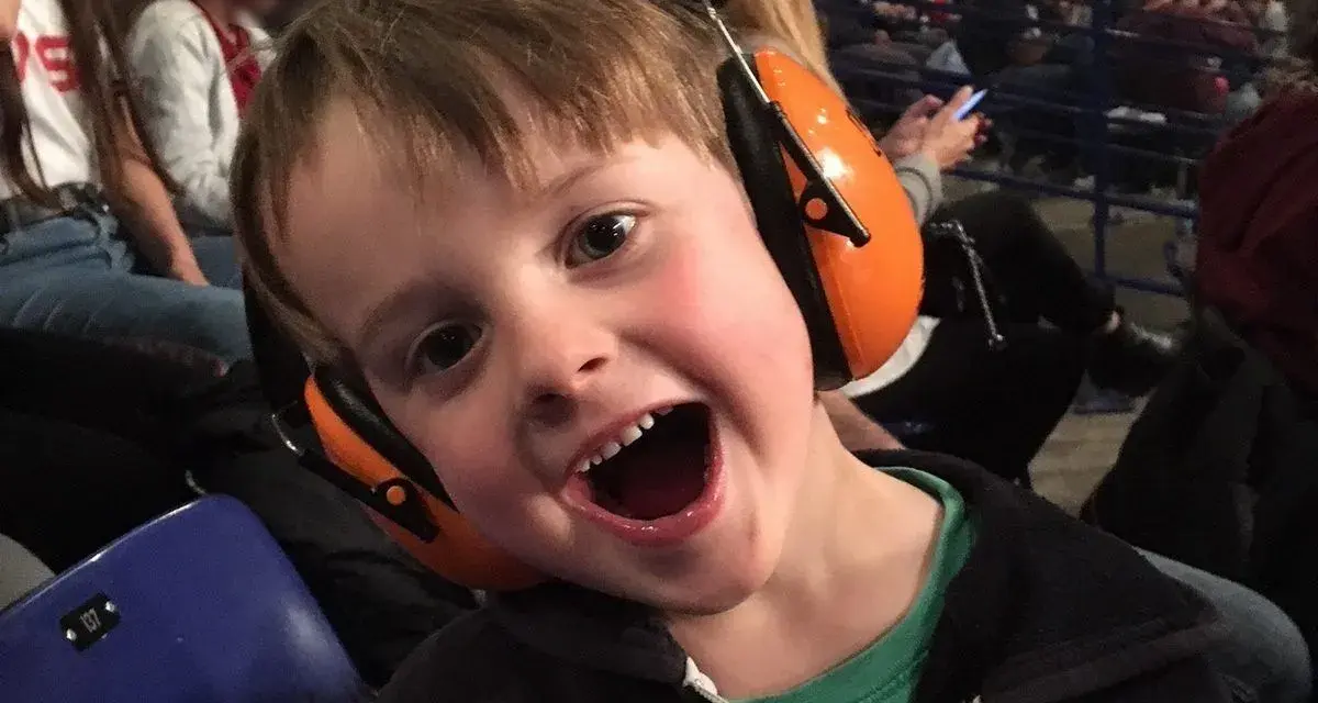 Un jeune garçon de 3 ans, avec un bouchon oreille enfant 3 ans, sourit à pleines dents, prêt pour le spectacle.