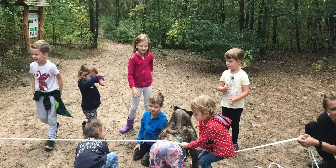Grupa dzieci w wieku 6-12 lat bierze udział w przeciąganiu liny w lesie. Wszyscy świetnie się bawią!