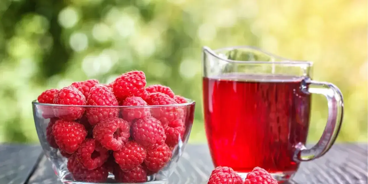 Świeże maliny w misce i dzbanek soku malinowego. Zastanawiasz się, ile pasteryzować sok z malin, by zachować jego smak i aromat?