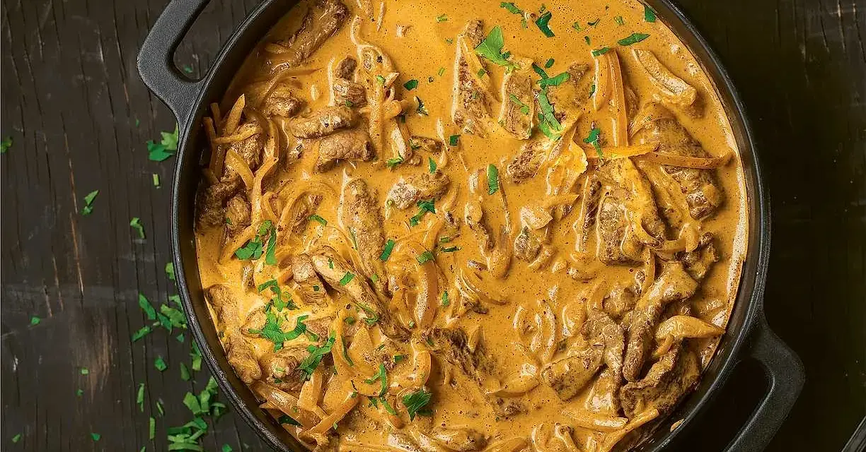 En gryta med krämig biff stroganoff, perfekt för ett mysigt middagsrecept. Garnerad med färsk persilja.