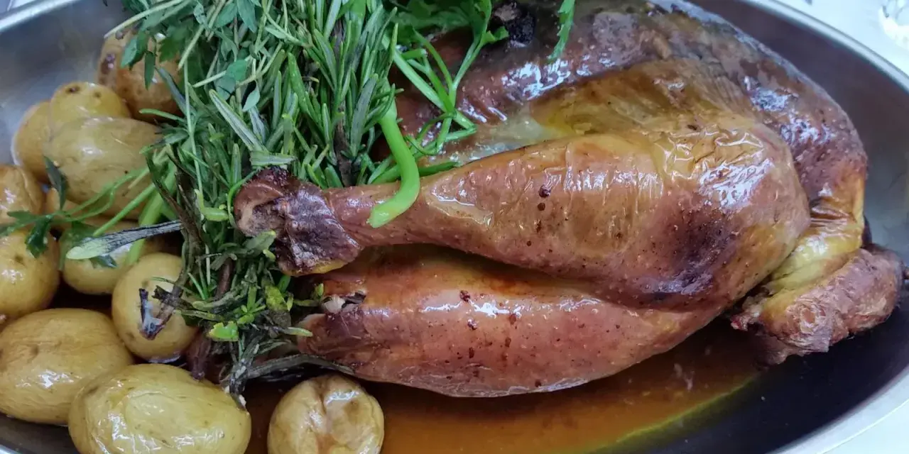 Pollo de Bresse asado, dorado y jugoso, acompañado de patatas pequeñas y hierbas frescas.