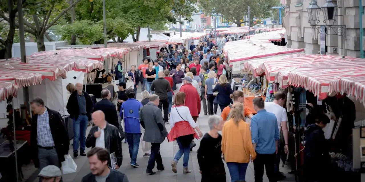 Menschen schlendern über einen belebten kunstmarkt berlin mit vielen Ständen und bunten Markisen.