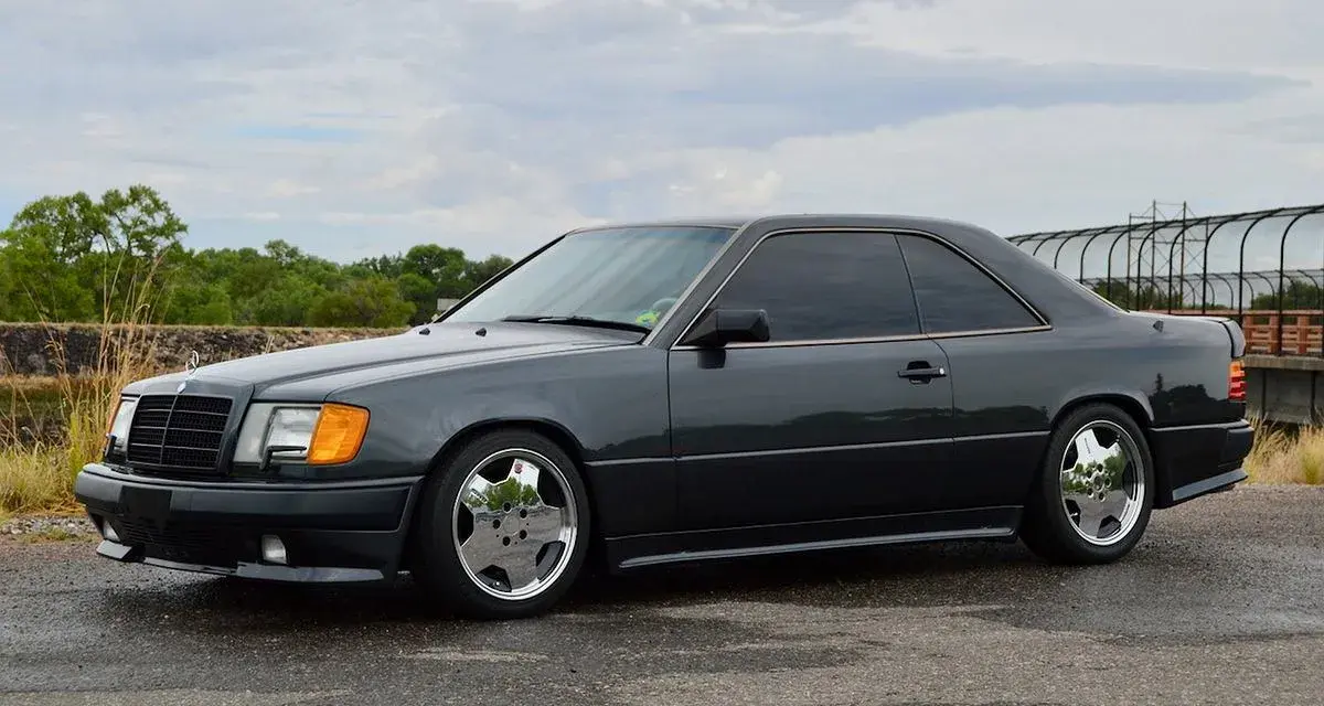 Ciemnoszary Mercedes "Hammer" coupe z przyciemnianymi szybami i chromowanymi felgami stoi na mokrej drodze.