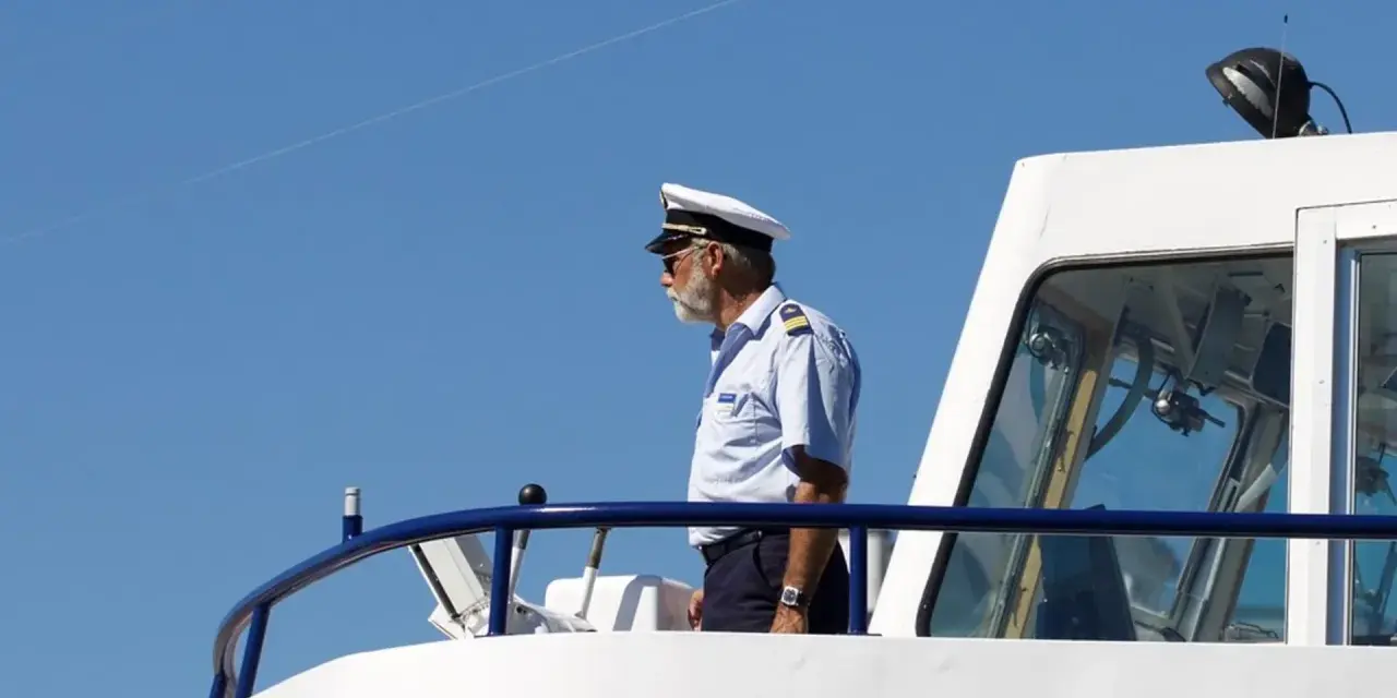 Kapitan na mostku statku, w białym mundurze i czapce, spogląda w dal. Zastanawiasz się, ile zarabia marynarz?
