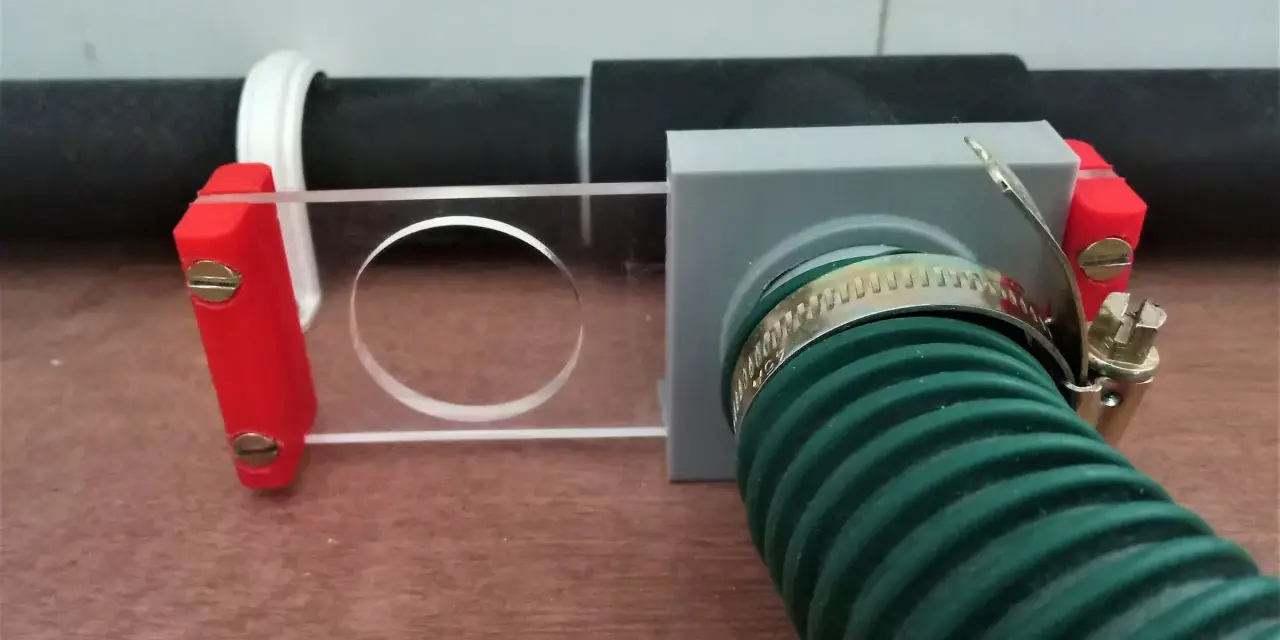 A 3d printed blast gate with a clear sliding mechanism and a green hose attached.