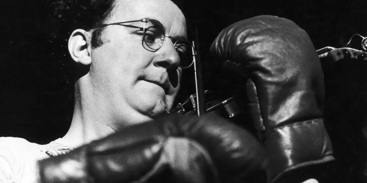 Coluche, lunettes rondes, gants de boxe, prêt à en découdre avec le racisme.