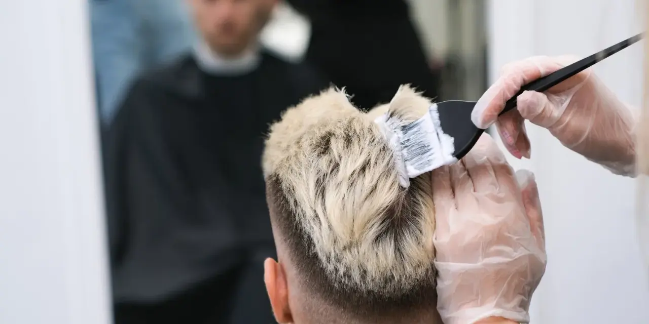 Fryzjer nakłada farbę na blond włosy mężczyzny.