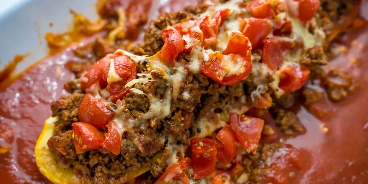 Herzhafte zucchini schiffchen gefüllt mit Hackfleisch, Tomaten und Käse, in einer aromatischen Tomatensauce.