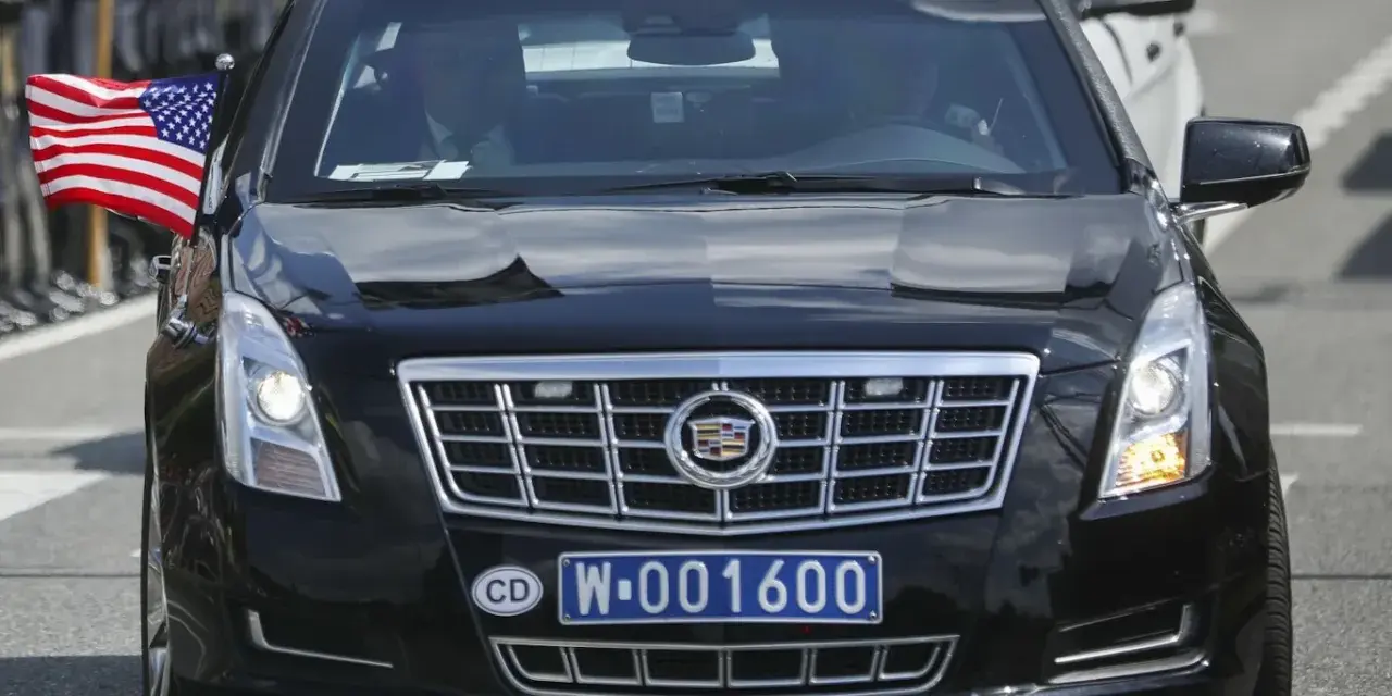 Czarny Cadillac z amerykańską flagą i tablicą rejestracyjną CD W-001600, wskazującą na rejestracje dyplomatyczne.