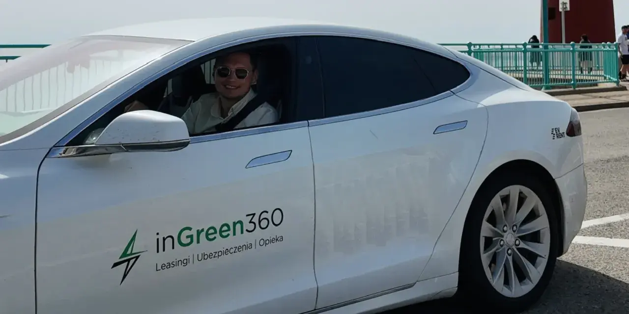 Uśmiechnięty mężczyzna w okularach przeciwsłonecznych siedzi za kierownicą białej Tesli z logo inGreen360.