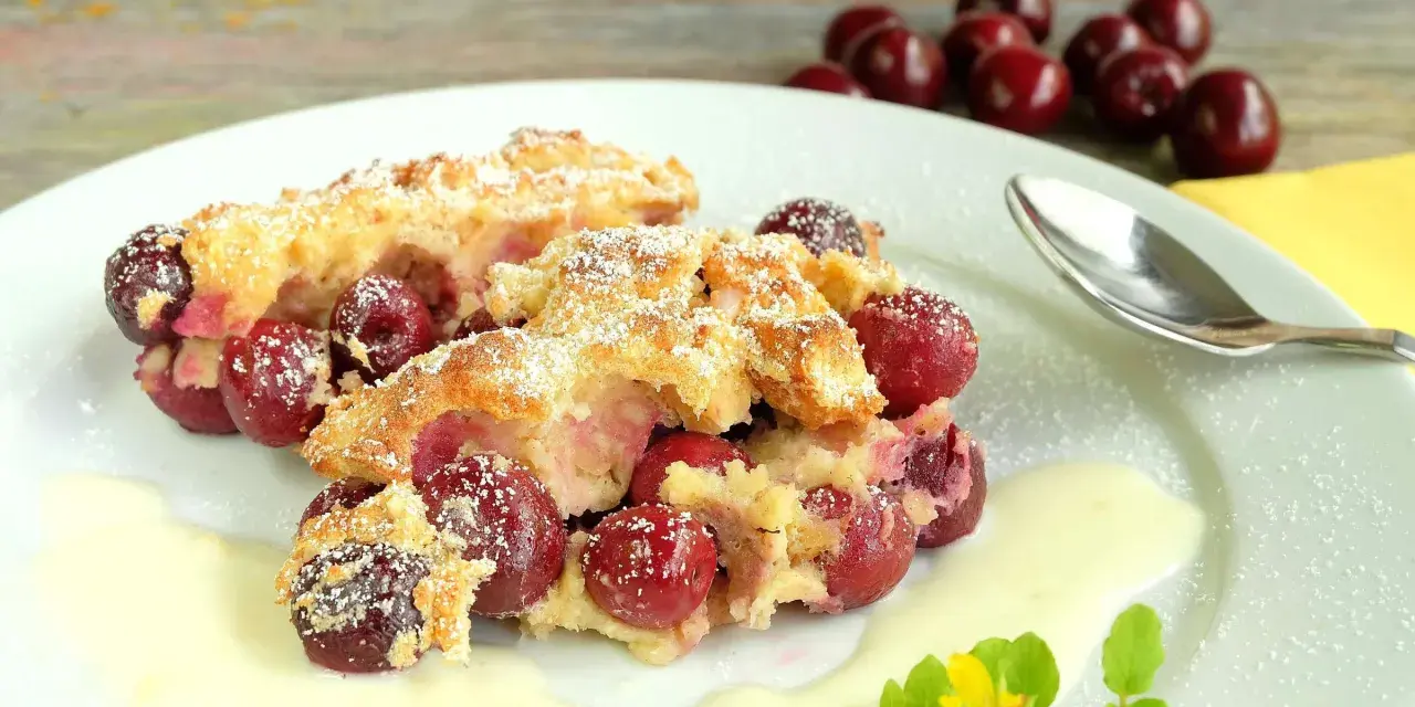Zwei Portionen Kirschenmichel, ein köstliches Dessert, serviert mit Vanillesauce und bestäubt mit Puderzucker. Ein perfektes Kirschenmichel Rezept.