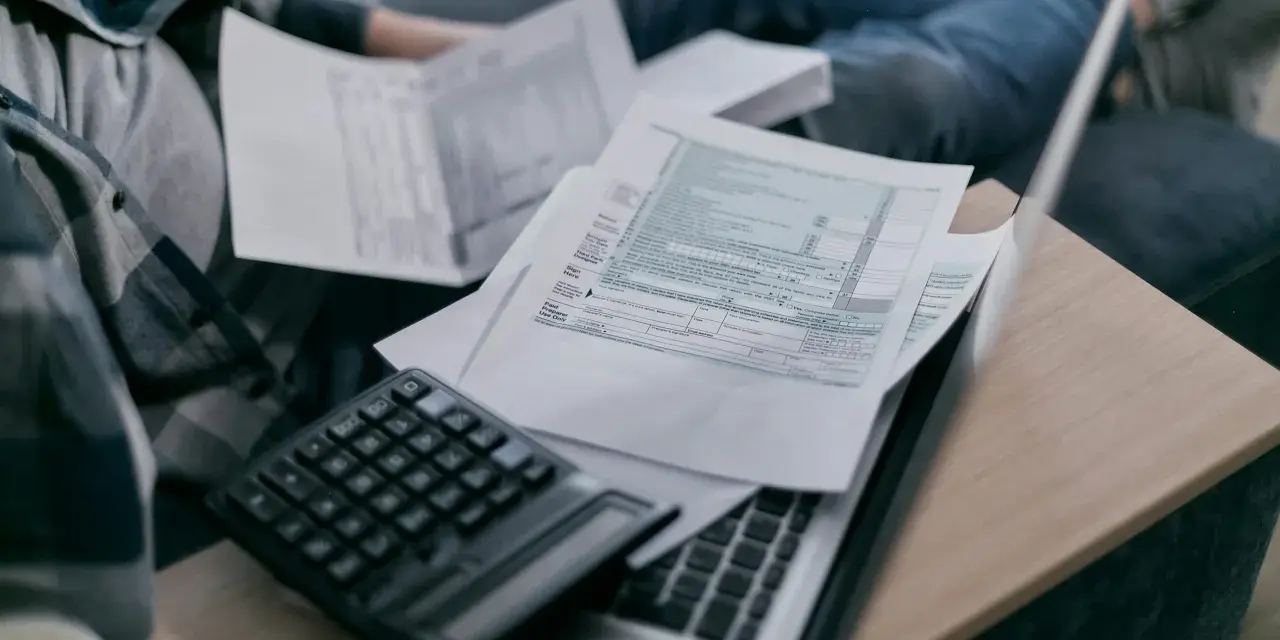 Osoba przegląda dokumenty podatkowe, kalkulator i laptop. Analiza składnik zmienny stawki sieciowej.
