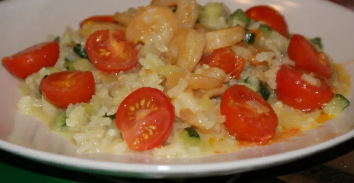 Risotto z krewetkami i pomidorkami koktajlowymi na białym talerzu.