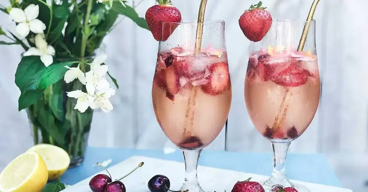 Två glas med ett uppfriskande drink med gin, fyllda med is, jordgubbar och körsbär. En perfekt sommardrink!
