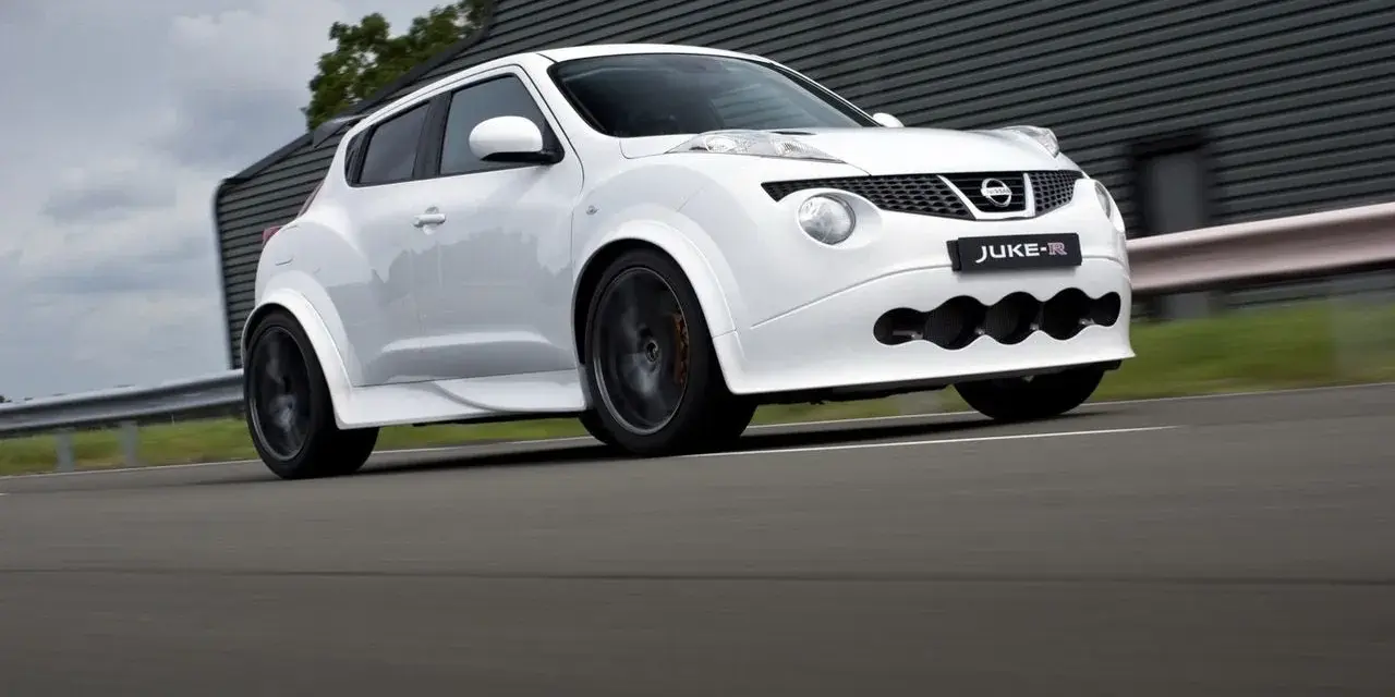 Biały Nissan Juke-R pędzi po torze, jego sportowy wygląd podkreślają szerokie nadkola i agresywny przedni zderzak.