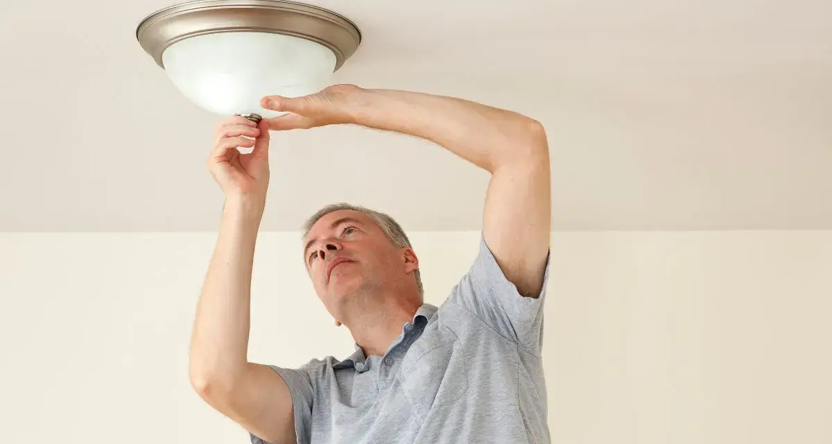 Mężczyzna wymienia żarówkę w lampie sufitowej, wykonując retrofit LED.