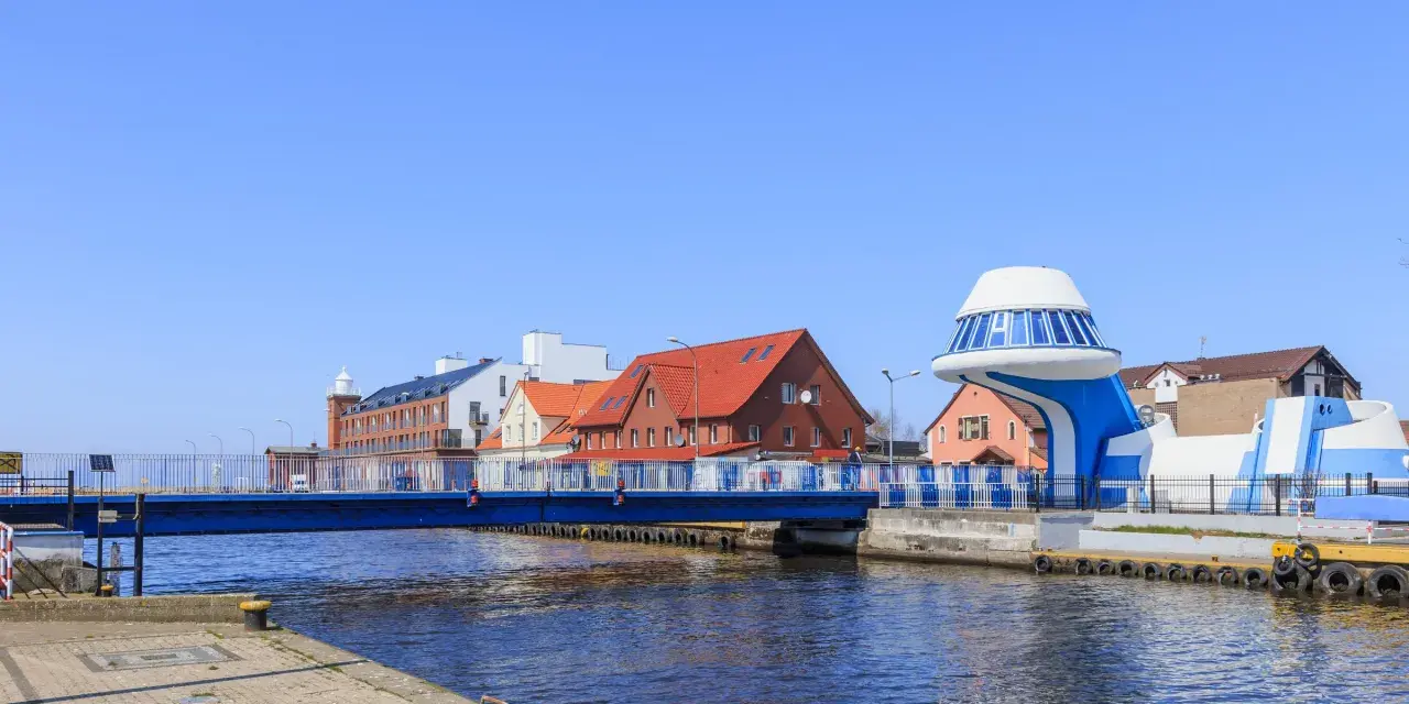 Port rybacki nad Wieprzą z niebieskim mostem i charakterystycznym budynkiem w kształcie statku kosmicznego.