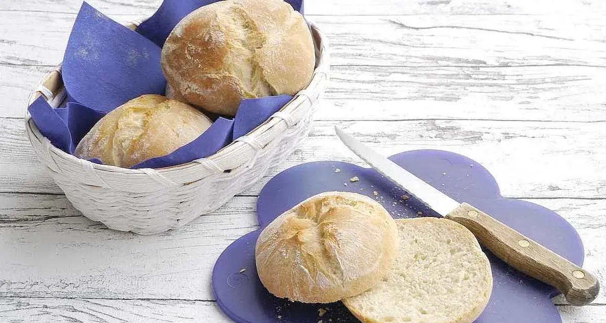 Frisch gebackenes, weiches Brot liegt in einem Korb und auf einem lila Brett. Ein Messer liegt daneben.