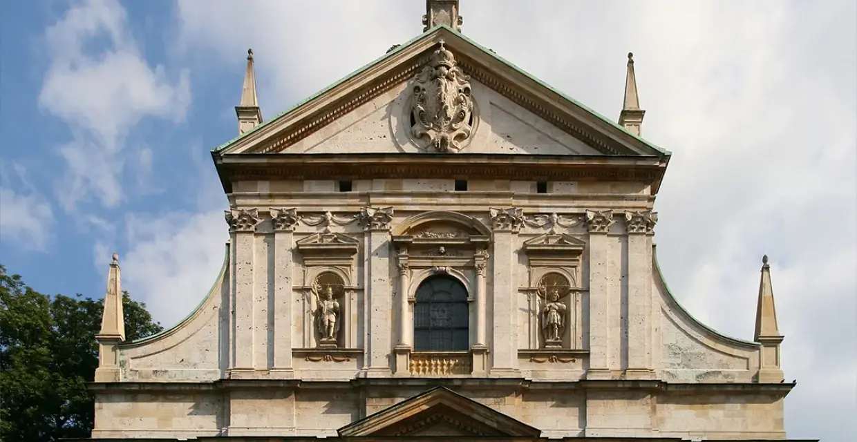 Bogata fasada kościoła w stylu barokowym, z rzeźbami i zdobieniami, pod błękitnym niebem.