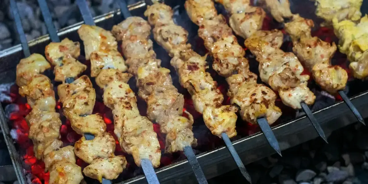 Aromatyczny kebab z kurczaka na rozżarzonych węglach. Soczyste kawałki mięsa pieką się na szpikulcach, tworząc apetyczny widok.