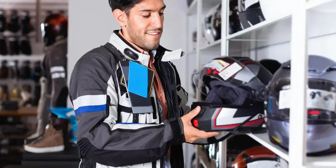 Uomo in negozio di moto esamina un casco, cercando la taglia XS. Corrisponde a una misura piccola, ideale per teste più minute.