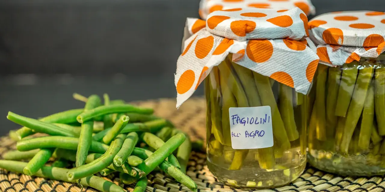 Fagiolini sott'olio in agrodolce, conservati in barattoli con tappi decorati. Freschi e pronti per essere gustati.