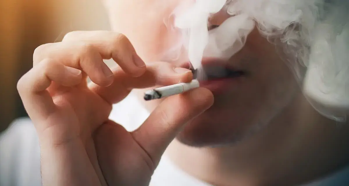 Persona fumando un cigarrillo, exhalando humo denso. Podría ser un indicio de sobredosis de nicotina.
