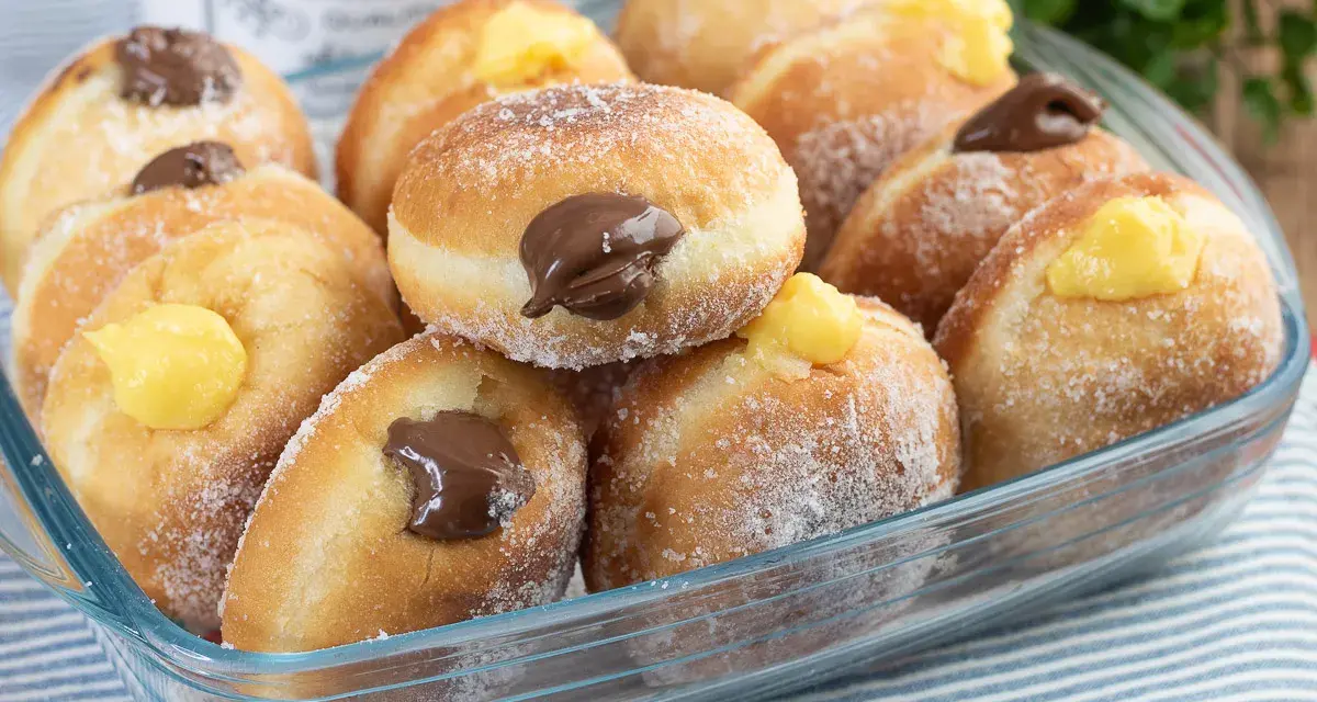 Bomboloni ricetta originale ripieni di crema e cioccolato, cosparsi di zucchero. Un dolce invitante pronto da gustare.