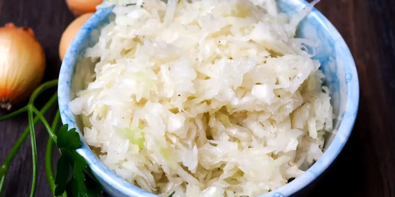 Schüssel mit frischem Krautsalat, daneben Zwiebeln und Petersilie. Perfekt für ein leckeres Krautsalat Rezept.