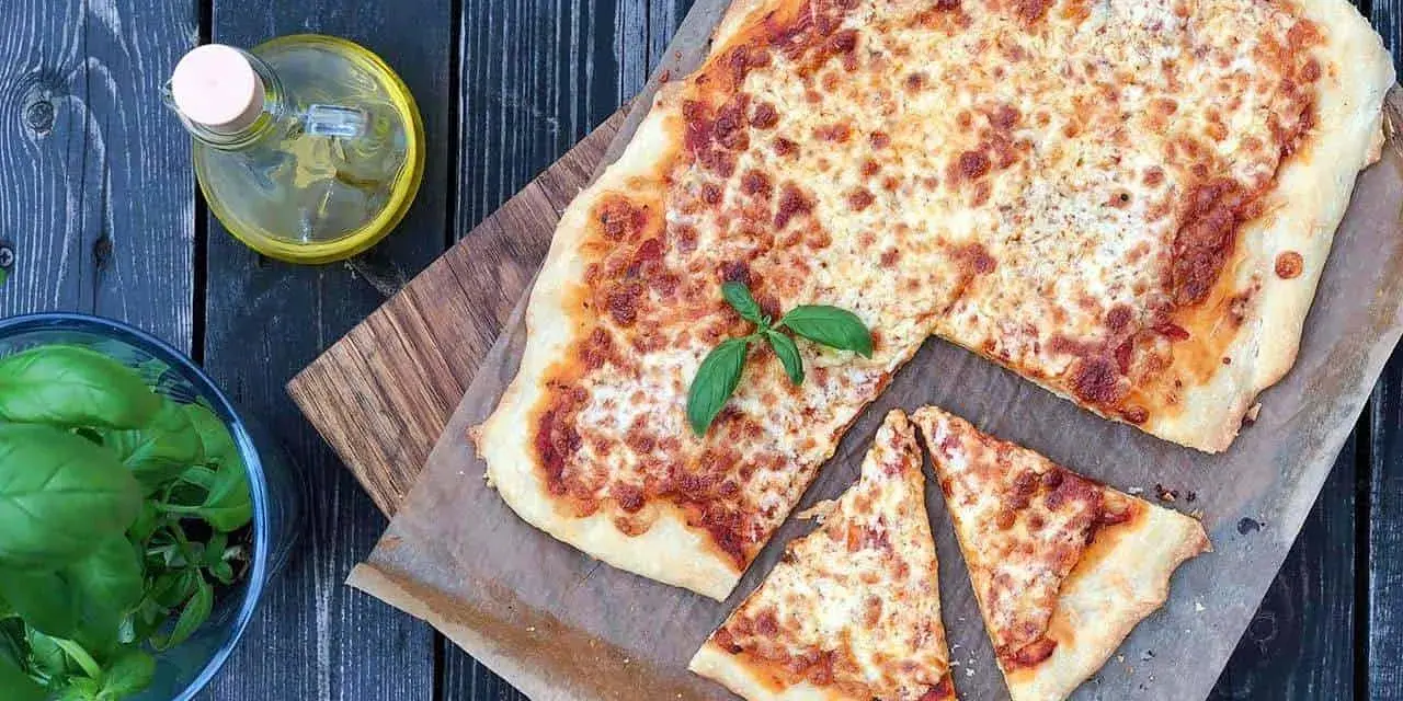 Pyszna pizza margherita z ciągnącym się serem i świeżą bazylią, obok butelka oliwy i miseczka ziół.