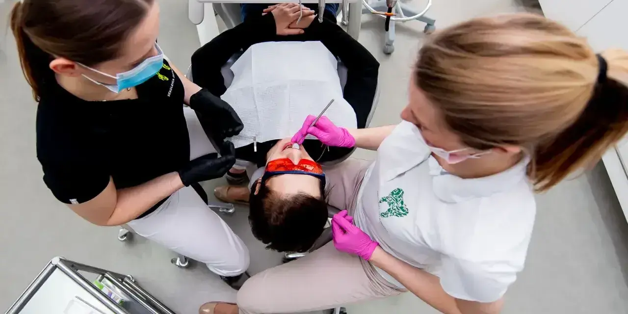 Dwie asystentki stomatologiczne pracują przy pacjencie. Zastanawiasz się, ile zarabia asystentka stomatologiczna?