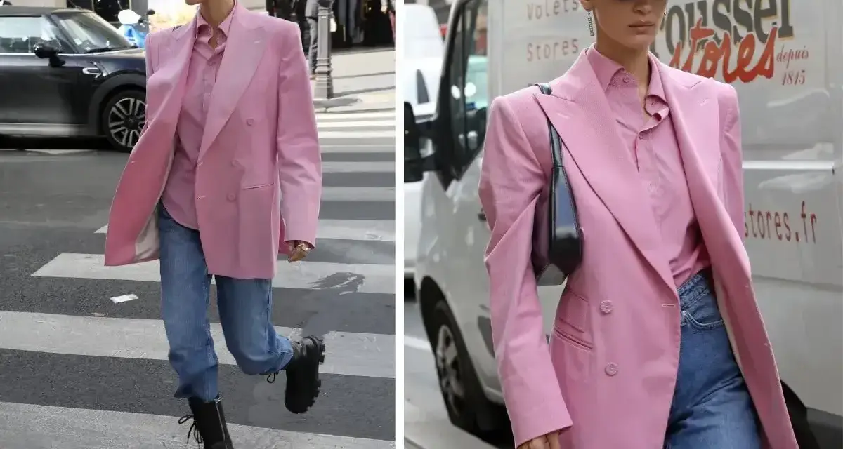 Kobieta w marynarce w odcieniu **magenta kolor** i jeansach idzie ulicą. Czapka z daszkiem i okulary dodają jej miejskiego stylu.