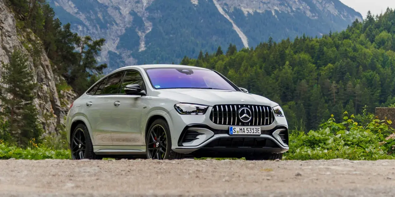 Biały Mercedes GLE 53 AMG coupe na tle górskiego krajobrazu z lasem.