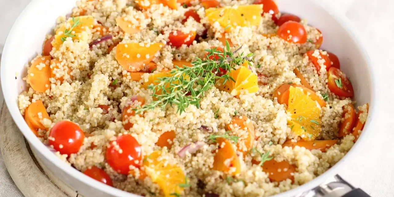 Salade de quinoa colorée avec carottes, tomates cerises et quartiers d'orange, garnie de thym. Un plat savoureux qui met en avant les quinoa bienfaits.