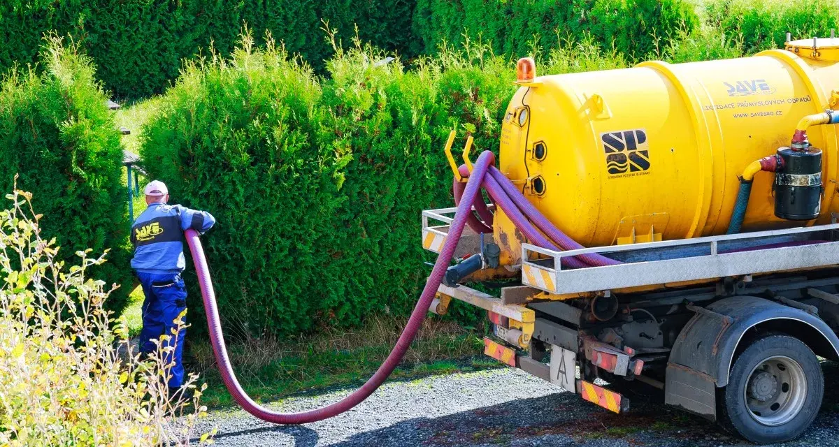 Pracownik podłącza wąż do żółtej beczkowozu. Sprawdź wywóz szamba cennik i zadbaj o czystość.