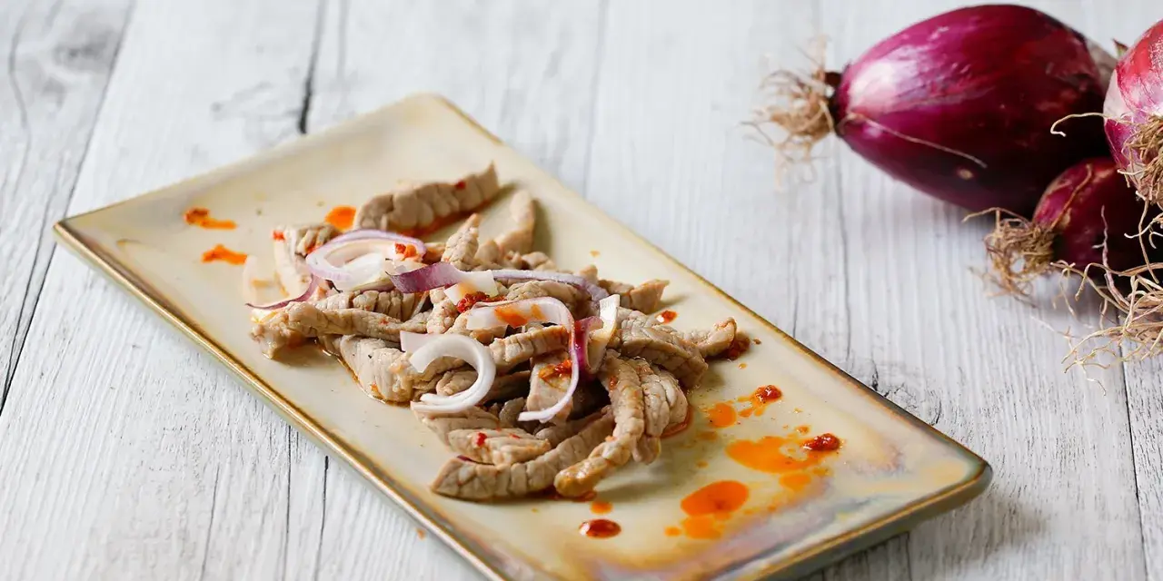 Straccetti di vitello conditi con cipolla rossa e un filo d'olio piccante, pronti per essere gustati.