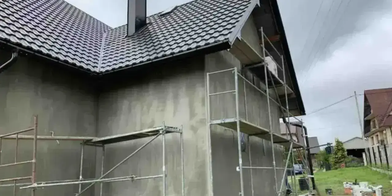 Dom w trakcie prac elewacyjnych. Widać rusztowania i szarą ścianę, która czeka na tynk silikonowy. Cena za m2 robocizny jest kluczowa dla budżetu.
