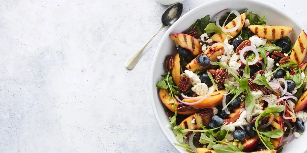 Salat mit Nektarinen, Blaubeeren, Feta und Pekannüssen. Gegrillte Nektarinenstücke und knackige Blätter bilden die Basis für diesen köstlichen Salat.