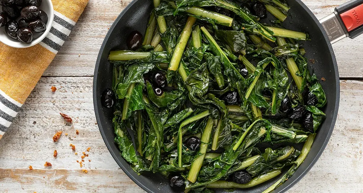 Verdura di catalogna saltata in padella con olive nere. Un piatto semplice e gustoso, pronto per essere servito.