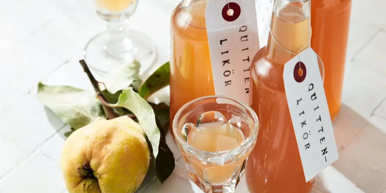 Flaschen mit selbstgemachtem Quittenlikör, daneben eine frische Quitte und ein Schnapsglas.