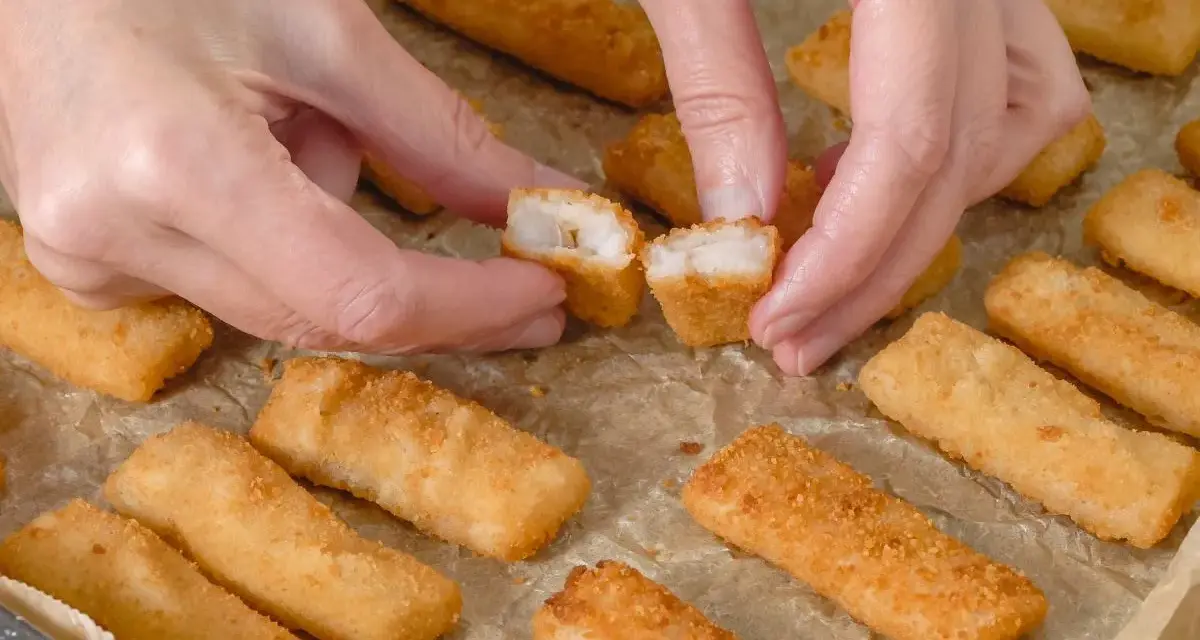 Ręce rozdzielają chrupiące paluszki rybne. Idealne na szybki obiad, warto sprawdzić paluszki rybne kcal.