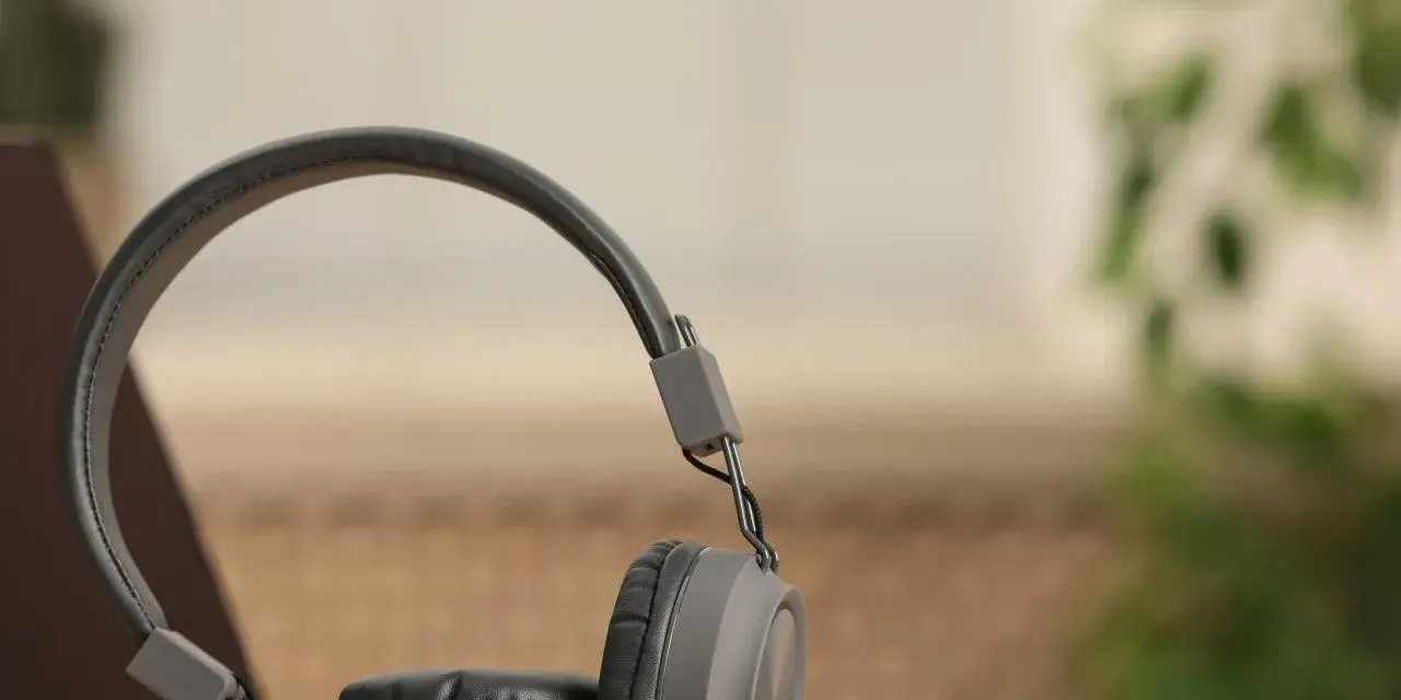 Szare słuchawki dynamiczne na drewnianym blacie, obok laptopa. Idealne do słuchania muzyki i podcastów.