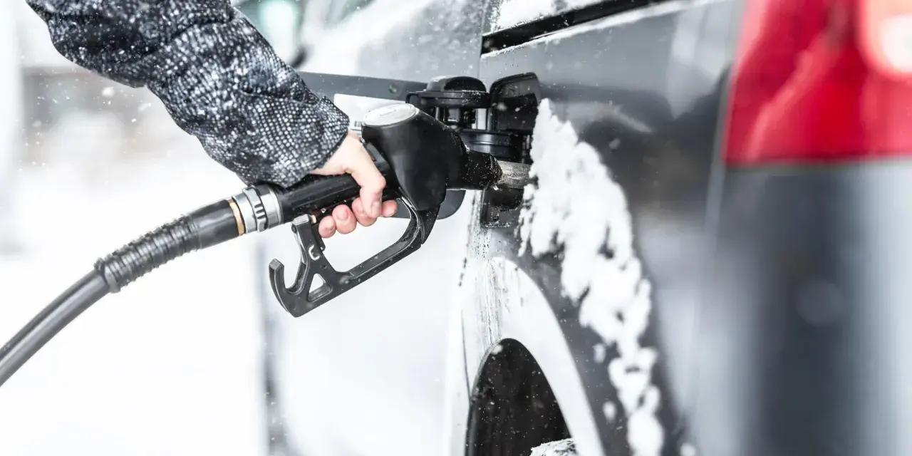 Ręka w zimowej kurtce trzyma pistolet do tankowania, nalewając diesel paliwo do samochodu podczas opadów śniegu.
