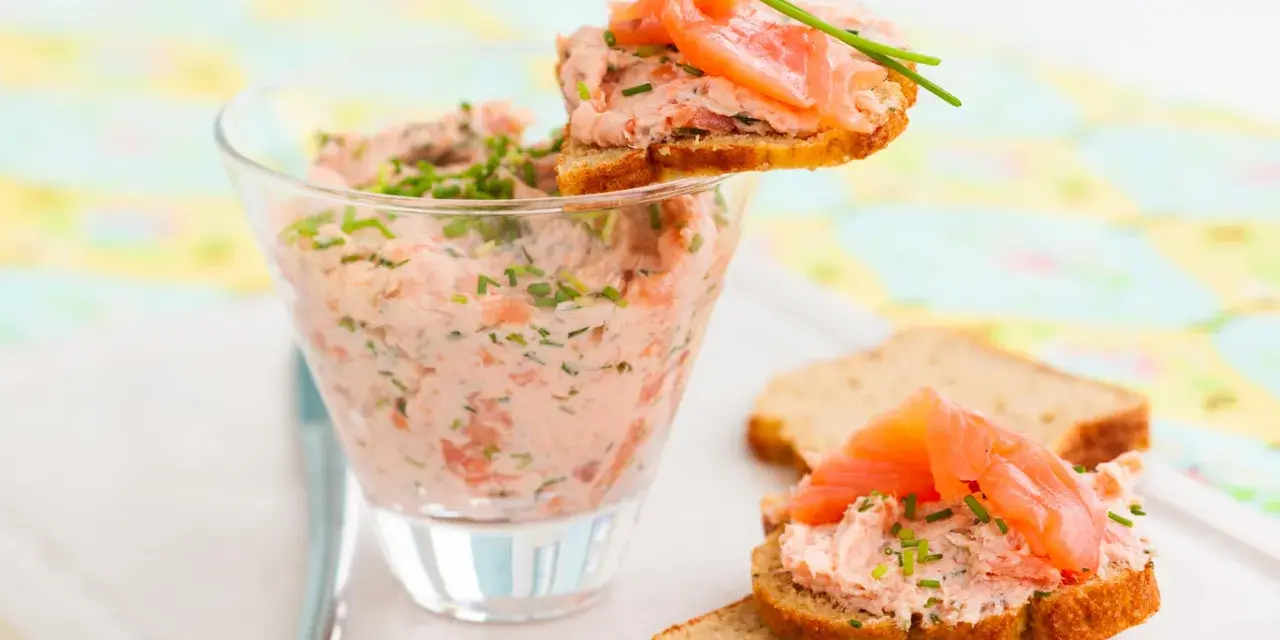 Rillettes de saumon crémeuses dans un verre, garnies de fines herbes et servies sur des toasts avec des tranches de saumon fumé.