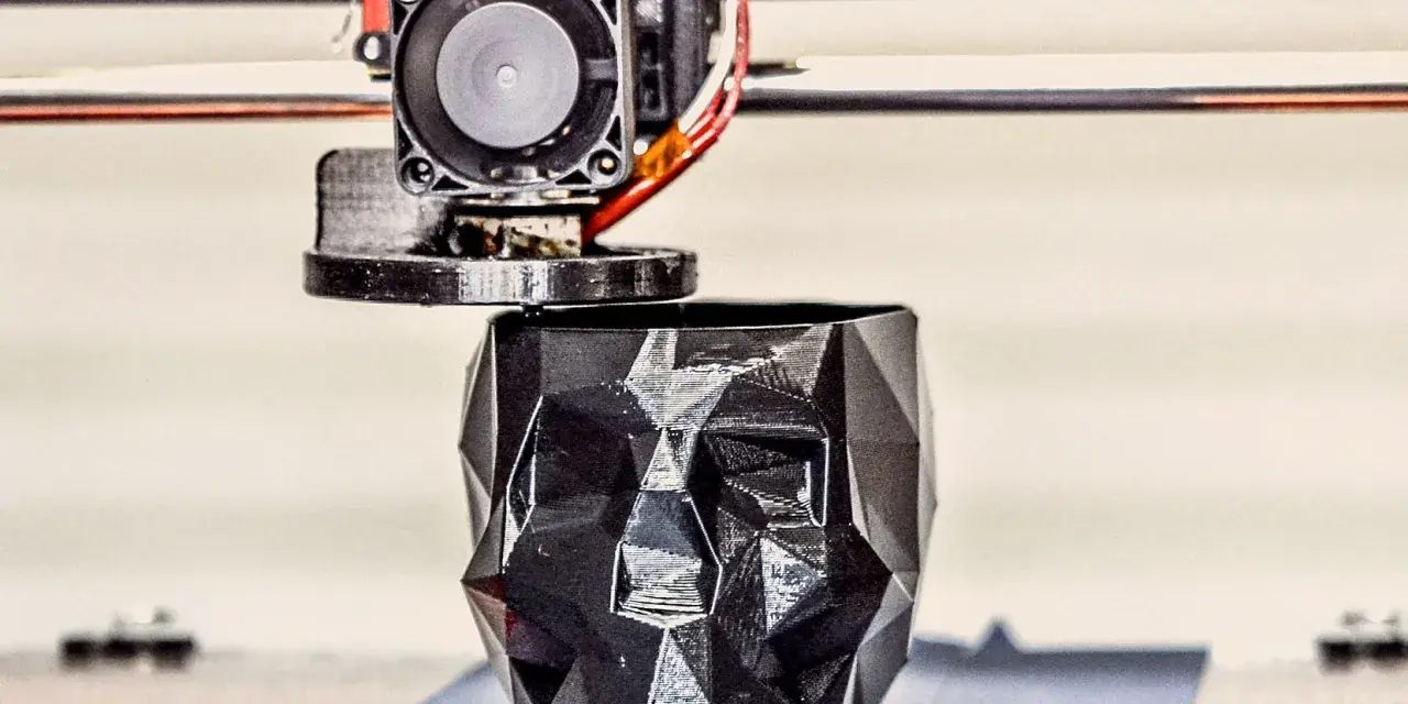 A 3D printer nozzle extrudes filament to create a faceted black skull planter, showcasing innovative 3D printing examples.