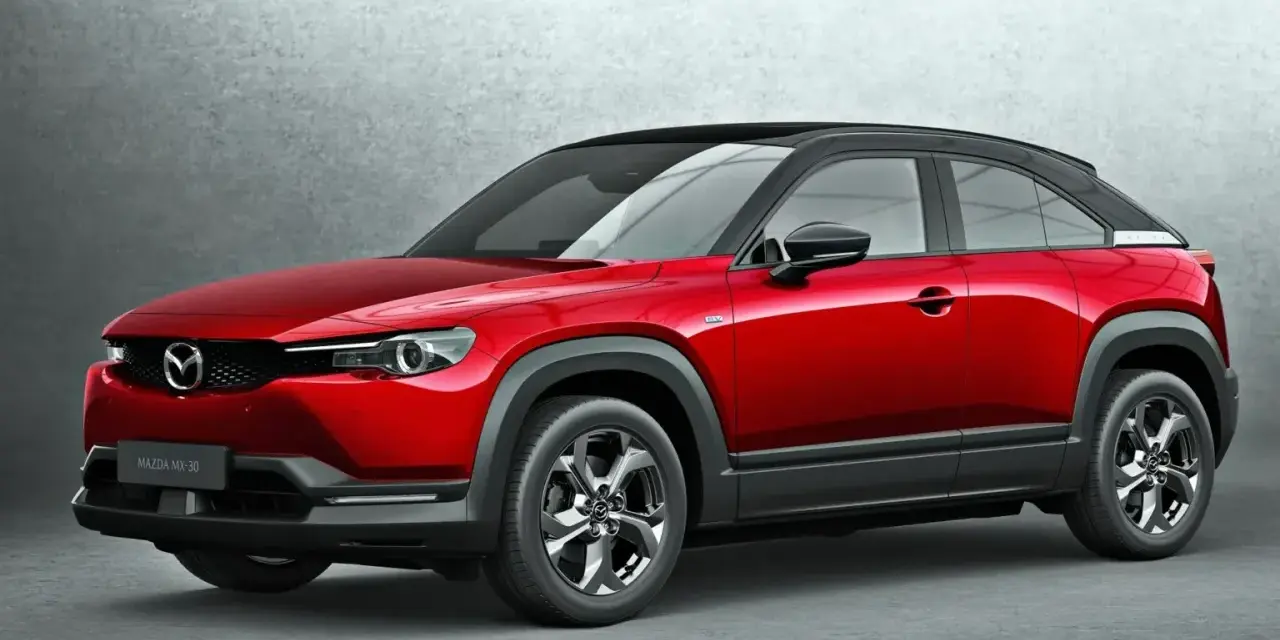 Czerwona Mazda MX-30 z czarnym dachem prezentuje się stylowo na tle szarej ściany.