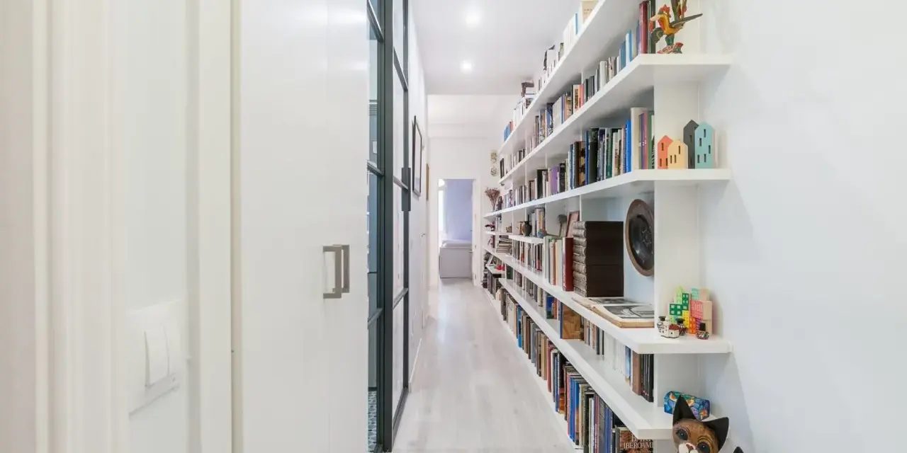 Pasillos estrechos y modernos con estanterías blancas repletas de libros y objetos decorativos, creando un ambiente acogedor.