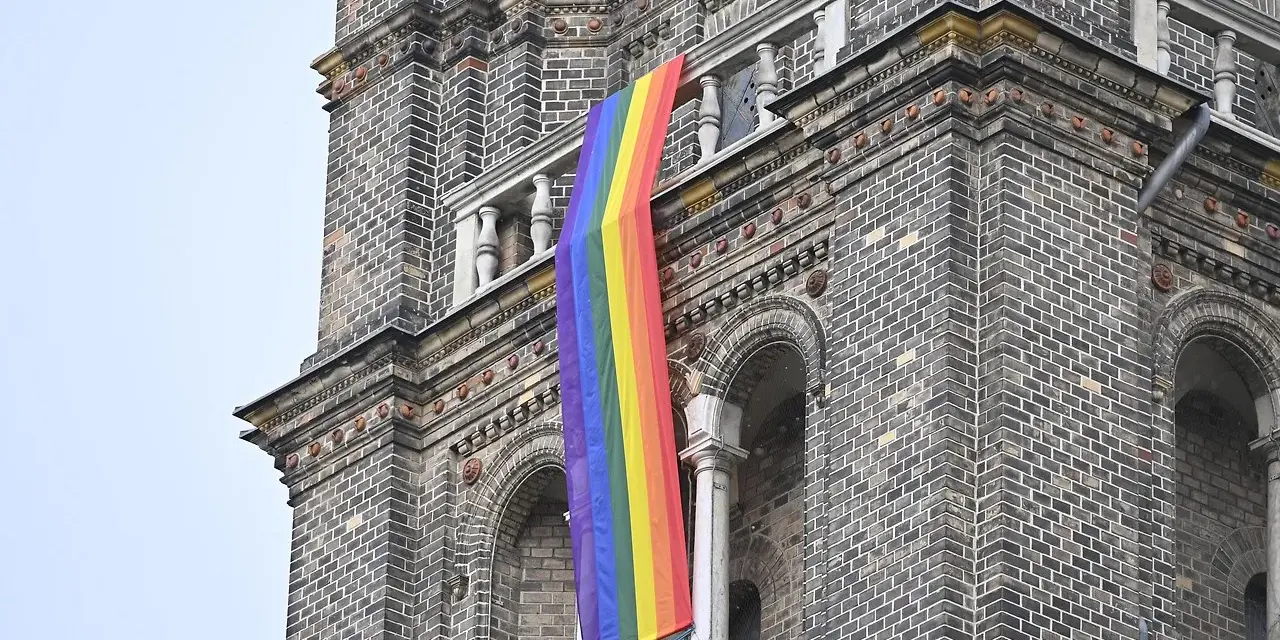 Regenbogenflagge hängt an einer Kirche. Die Bedeutung der Regenbogenflagge steht für Vielfalt und Akzeptanz.