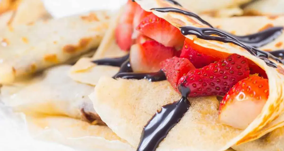 Deliziose crepes senza burro, ripiene di fragole fresche e ricoperte da una golosa salsa al cioccolato.